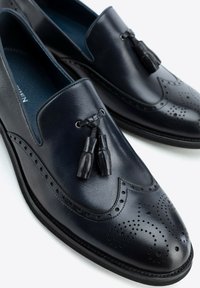 Black leather men's loafers with tassels and decorative perforations on the toe and sides, displayed on a white background.
