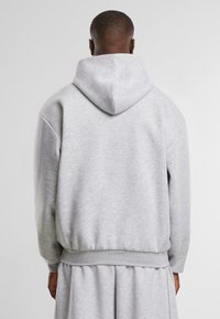 Grey hoodie with a large hood, ribbed cuffs and hem, and a relaxed fit. Soft texture with minimal seams, worn over a matching garment.
