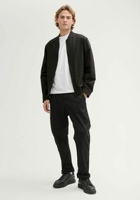 Czarna kurtka bomberka na białym t-shircie, zestawiona z czarnymi zwężanymi spodniami i masywnymi czarnymi sneakersami. Gładki materiał, minimalistyczny design.