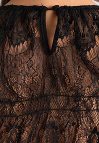 Blusa nera in pizzo con una texture trasparente, motivi floreali e un'apertura a chiave sul retro fissata con un bottone. Design delicato e dettagliato.
