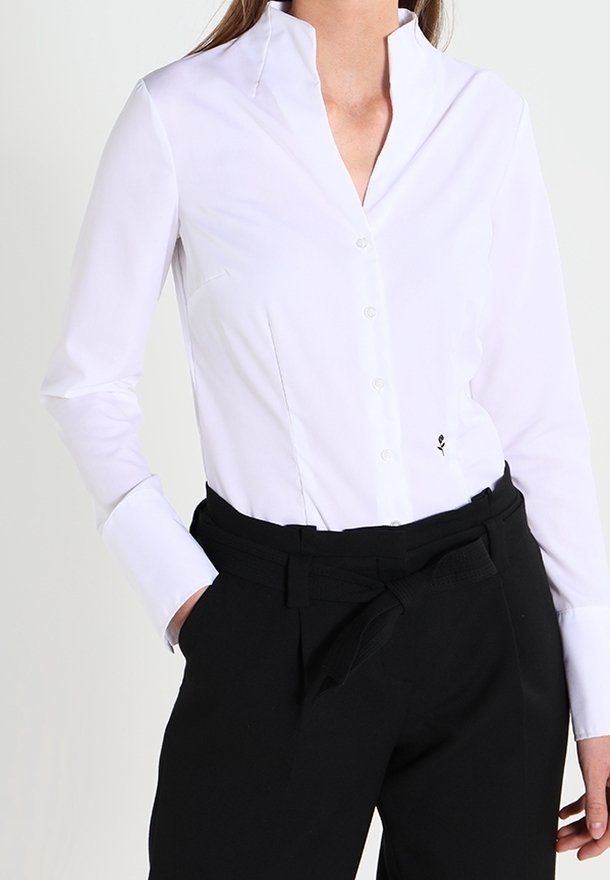Weißes Hemd mit Stehkragen, langen Ärmeln und taillierter Passform. Kombiniert mit hoch taillierten schwarzen Hosen mit einem Gürtel.