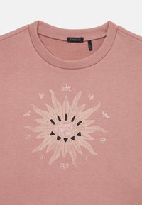 T-shirt in cotone rosa chiaro con una grafica testurizzata del sole in crema e nero, con dettagli glitterati e elementi decorativi più piccoli.