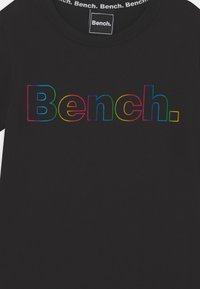 Czarna koszulka z logo "Bench." w dużych, pogrubionych literach, obrysowanych tęczowym gradientem na klatce piersiowej.