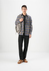 Plaid shirt in blue and yellow tones, black t-shirt, dark jeans, brown textured sneakers, and a grey messenger bag with zip details.
