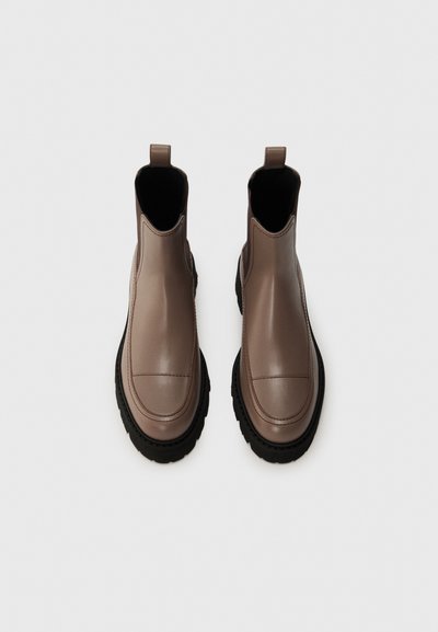 Stivali chelsea in pelle di colore taupe con finitura liscia. Presenta pannelli laterali elasticizzati e una robusta suola in gomma nera per una migliore aderenza.