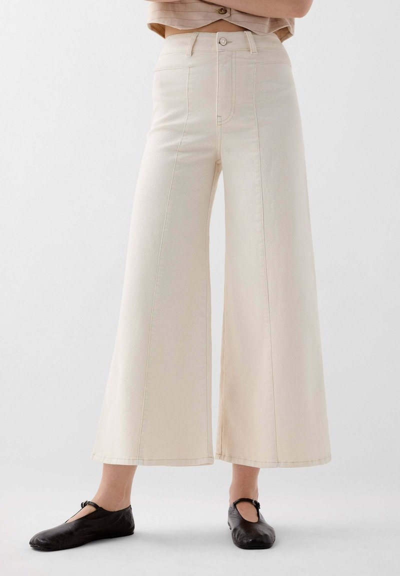 Beige wijde broek van denim met een hoge taille, voorzien van een knoopsluiting aan de voorkant en zijzakken. Gladde textuur, strak design.