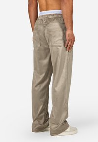 Light gray, soft fabric joggers with a relaxed fit, elastic waistband, and two back pockets. Smooth texture with minimal detailing.