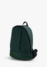 Mochila de color verde oscuro con forma redondeada, textura suave, bolsillo delantero con cremallera y correas ajustables negras. Diseño minimalista y detalle de logo.