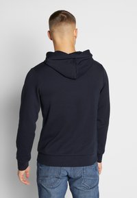 Mörkblå hoodie i mjukt tyg, med en känguruficka och en justerbar huva, tillsammans med ljusblå jeans.