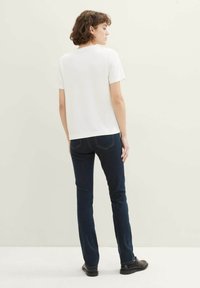 T-shirt blanc à manches courtes associé à un jean en denim bleu foncé. Le tissu semble lisse, avec des coutures simples et une coupe classique.