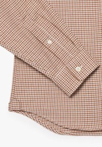 Camisa de cuadros marrón y blanca con mangas largas, puños abotonados, dobladillo curvado y textura de tela suave. Los puños están acentuados con botones blancos.