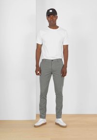 Witte t-shirt, lichtgrijze broek en witte sneakers. Glad stof met een aansluitend ontwerp. De pet is zwart met een vierkant logo.