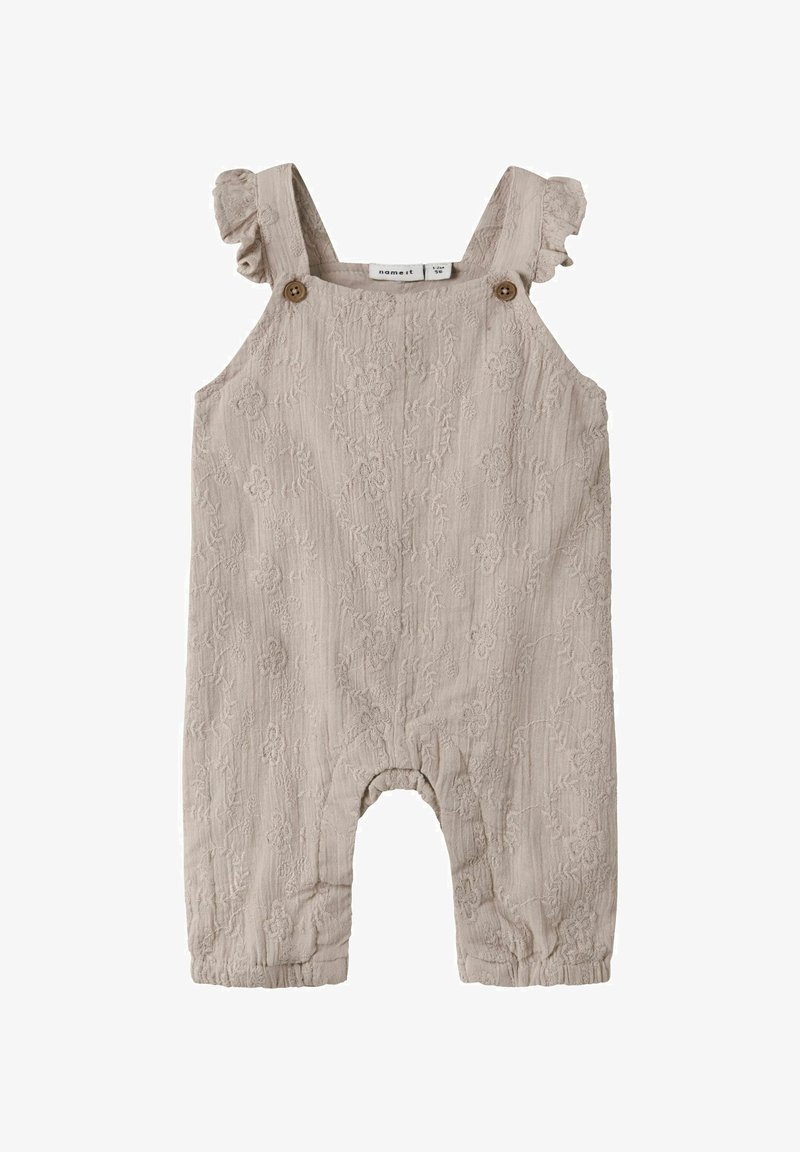 Barboteuse bébé beige texturée avec broderie florale, bretelles à volants et détails de boutons en bois sur fond blanc.
