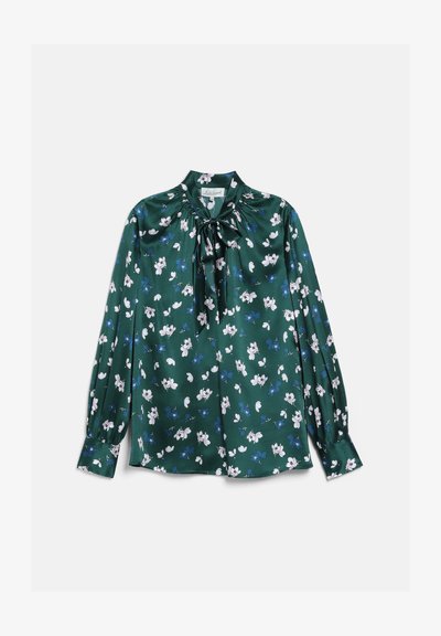 Blouse vert foncé à manches longues avec motif floral blanc et bleu, détail nœud haut de col, et poignets boutonnés, posée à plat sur fond blanc.