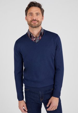 Suéter de pico azul marino hecho de tejido de punto, superpuesto a una camisa de cuadros gris con cuello, con mangas largas y puños y dobladillo acanalados.