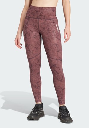 Terrex maroon leggings with a textured pattern, high waist design, and contrasting seams, paired with black athletic shoes.