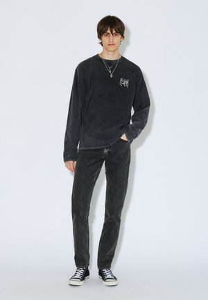 Langärmliges, dunkelgraues Shirt mit Frontgrafik, kombiniert mit dunklen Jeans und schwarzen High-Top-Sneakern. Einfaches Design, lässige Passform, minimale Details.