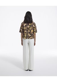Blusa a maniche corte con un motivo floreale multicolore su uno sfondo scuro, abbinata a pantaloni bianchi a vita alta e larghi.