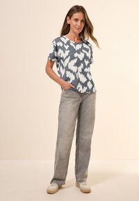 T-shirt à manches courtes avec un motif abstrait bleu et blanc ; coupe décontractée. Associé à un jean large gris clair et des baskets blanches.