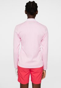 Långärmad rosa skjorta i strukturerad tyg, kombinerad med ljusa korallfärgade shorts. Har en krage och vit kantdetalj nära halsringningen.