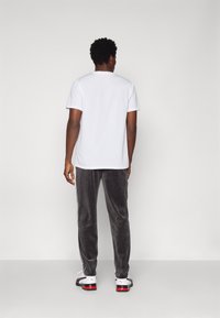 Biała koszulka z krótkim rękawem i szare spodnie z weluru z białymi paskami po bokach, noszone z czarno-białymi trampkami. Miękka tkanina, luźny krój.