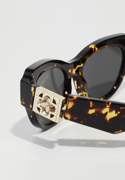 Occhiali da sole tartarugati con lenti grigie scure. Presentano un accento in metallo dorato sulla asticella con un design floreale. Struttura della montatura spessa.