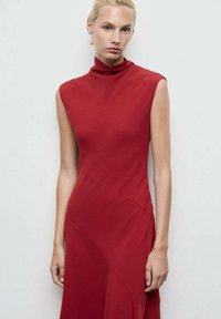 Rochie roșie, fără mâneci, cu gâtul înalt și ajustat. Fabricată dintr-un material fin, prezintă o cusătură diagonală și o siluetă în linie A.