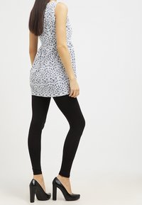 Sininen ja valkoinen kuvioitu hihaton tunikapaita, jonka kanssa on mustat legginsit ja mustat korkokengät. Sujuva kangas, jossa on liehukehous.