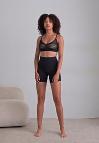 Svart blondebralette med tynne stropper, sammen med høyt liv svarte shorts. Glatt tekstur, minimalistisch design og figursydd fasong.