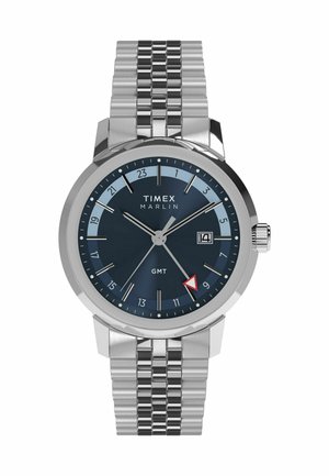 Montre Timex Marlin avec un bracelet en acier inoxydable, un cadran bleu foncé, des accents argentés, un affichage de la date et une aiguille GMT triangulaire rouge.