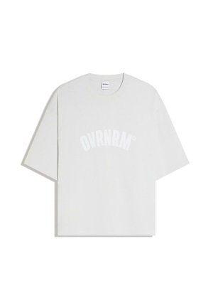 Witte oversized T-shirt met korte mouwen en een ronde hals, met "OVRNRM" in grote, gebogen witte letters op de voorkant gedrukt.