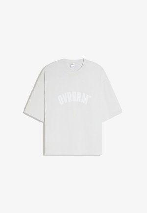 Witte oversized T-shirt met korte mouwen en een ronde hals, met "OVRNRM" in grote, gebogen witte letters op de voorkant gedrukt.