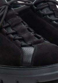Czarne sneakersy wykonane z zamszu i teksturowanej skóry. Posiadają okrągły czubek, grubą czarną podeszwę oraz sznurowanie z płaskimi sznurówkami.