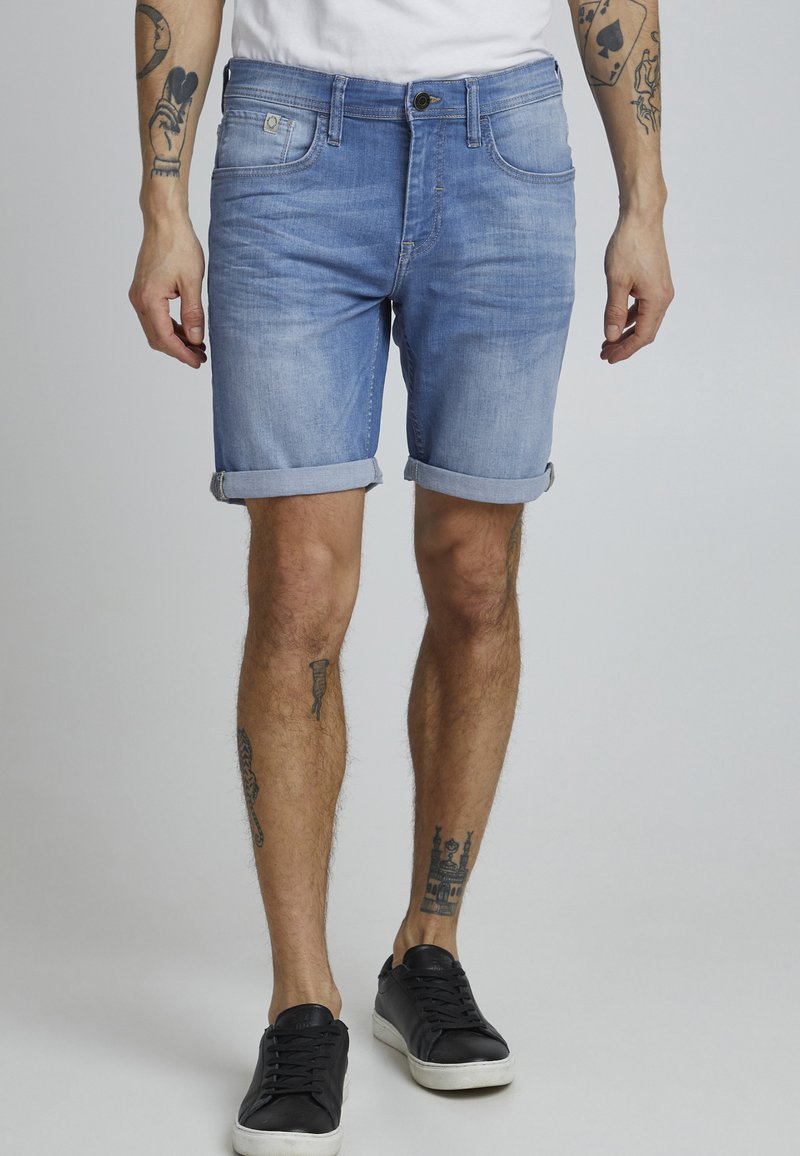 Shorts de mezclilla azul claro con dobladillo enrollado, corte recto y diseño de cinco bolsillos. Combinados con zapatillas negras.