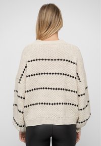 Kremowy sweter z dzianiny z czarnym paskowanym wzorem, w oversize'owym kroju, okrągłym dekolcie oraz ściągaczami przy mankietach i dolnej części. Teksturowany, casualowy design.