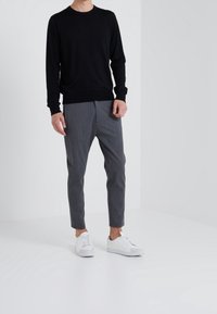 Svart långärmad tröja, grå randiga byxor och vita sneakers. Outfiten har en figurnära design med en jämn textur.