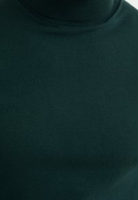 Mörkgrön ribbad polotröja som visar en närbild av tygtexturen och kragen.