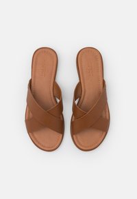 Sandales marron à brides croisées avec une finition texturée, dotées d'une semelle intérieure en cuir lisse et de détails de couture subtils. Conception ouverte, semelle plate.