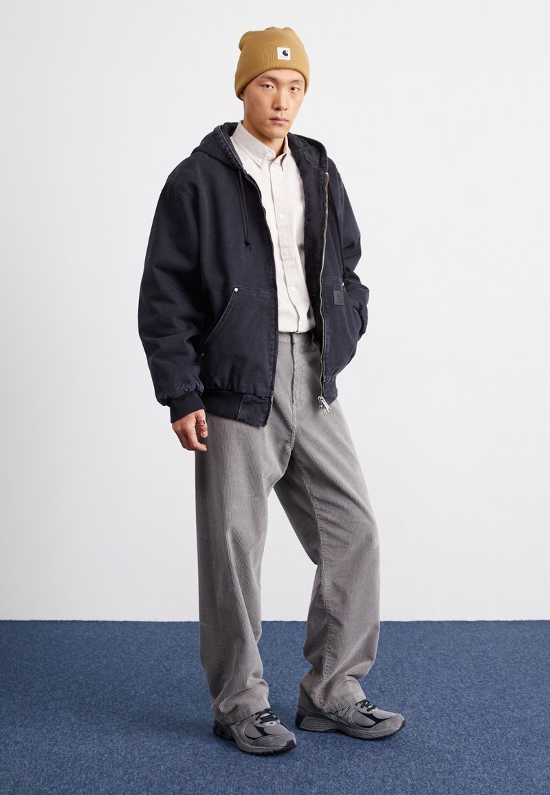 Veste à capuche bleu foncé, beige bonnet, chemise claire à boutons, pantalon en côtes de velours gris et baskets grises avec des accents noirs.