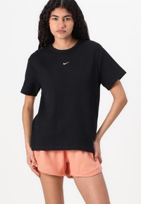 Black ribbed t-shirt with a round neckline and short sleeves, featuring a white Nike logo, paired with light peach ribbed shorts.