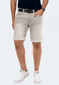 Helle graue Jeansshorts mit umgeschlagenen Säumen, ausgestattet mit Fronttaschen und einem schwarzen Gürtel. Getragen mit weißen Sneakers und Socken mit grauen Akzenten.