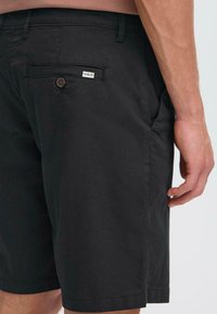 Black cotton shorts with a straight leg design, featuring a rear pocket and a brown button. Label on pocket reads "ISOLID." Smooth texture.