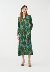 Abito floreale lungo e verde con accenti blu, dotato di maniche lunghe, scollatura a V e tasche laterali. Tessuto morbido con un design fluido.