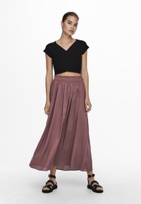 Zwarte cropped top met korte mouwen; vloeiende, mauve enkel-lange rok; zachte stof met een geraffineerde tailleband; gecombineerd met zwarte strappy sandalen.