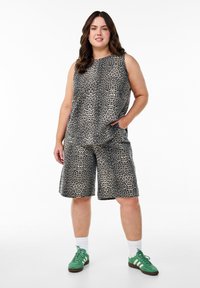 Mouwloze top met luipaardprint, gecombineerd met knielange shorts, beide in een beige en zwart patroon, gedragen met groene sportschoenen.