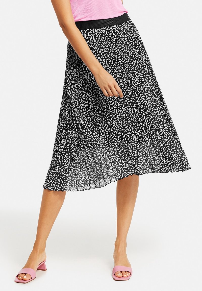 Jupe noire plissée à motifs abstraits blancs, dotée d'une taille élastique et d'une coupe fluide. Accompagnée de sandales roses à enfiler.