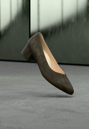 Chaussure femme en daim brun foncé à petit talon, affichée en angle sur un fond intérieur flou.
