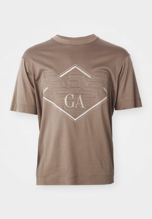 Bruine T-shirt met korte mouwen, voorzien van een gestikt geometrisch embleem en de letters "GA" gecentreerd op de borst.