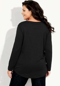 Czarna koszula z długim rękawem, zaokrąglonym dołem i luźnym krojem. Posiada szeroki dekolt i miękką fakturę, zestawiona z ciemnymi dżinsami.