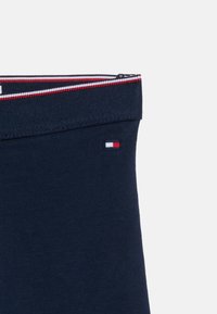 Λωρίδα μέσης από ύφασμα σε ναυτικό μπλε, με ελαστική φάσα σε ρίγες κόκκινου, λευκού και ναυτικού μπλε και μικρό λογότυπο με σημαία σε κόκκινο, λευκό και ναυτικό μπλε.